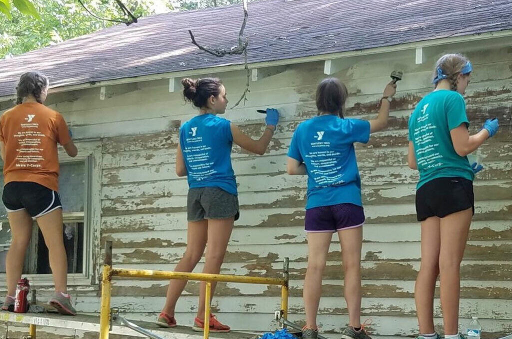 Students standing on scaffolding painting a building.